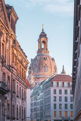Fototapeta premium Frauenkirche stands tall in Dresden. The view captures the church's dome rising above nearby buildings. It is early morning, and the sky is clear. Visitors explore the area and take photos.