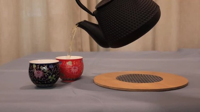 Chinese tea with two teacups. Traditional tea serving and tea preparation concept. Hot tea poured into ceramic cups, close-up view of tableware and beverage. Asian culture, tea ceremony, calm atmosphe