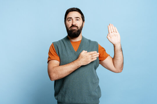 Serious pensive bearded man holding hand up and on chest promise telling the truth