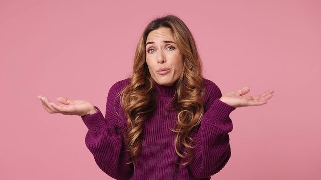 Hesitant indecisive fun shy young woman she wear purple knitted sweater casual clothes feels doubtful spreading hands say oops ouch oh omg i am so sorry isolated on plain pastel light pink background