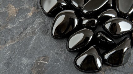 Close up of polished black obsidian shards with a smooth shiny surface on a textured dark background