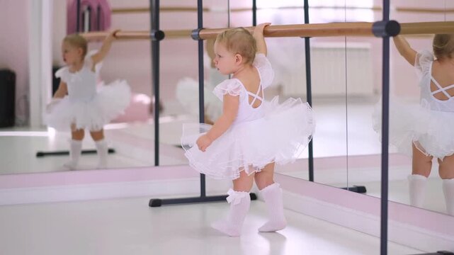 Moscow, Russia,04.04.2024 Little girl in white tutu outfit holding onto ballet barre in dance studio for childrens developmental activity