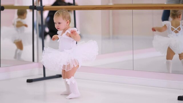 Moscow, Russia,04.04.2024 Cute baby girl in white tutu dress standing in ballet studio with mirror. Childhood dancing training and dream concept.