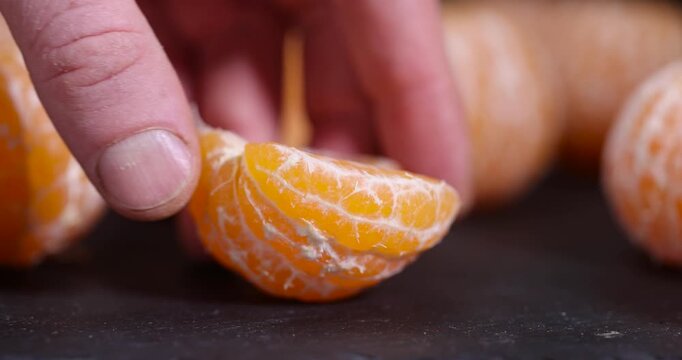 sliced juicy orange tangerine on a black slate table, ripe orange small mandarin without peel on a black slate board, tangerine divided into small slices