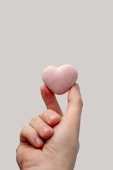Hand holding up a small, delicate pink heart-shaped macaron, symbolizing love, romance, and sweet gestures for Valentine's Day or an anniversary celebration