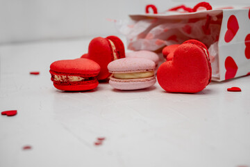 Heart-shaped red and pink macarons are spilling from a white gift bag decorated with red hearts, representing love, romance, and sweet treats for a special occasion