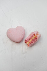 Pink heart-shaped macarons, one whole and one bitten showing a creamy filling, representing concepts of love, romance, and sweet indulgence on a textured white background with copy space