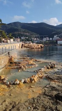 Natural hot springs flowing into the sea in Loutra Edipsos, Evia Island, Greece. Scenic coastal landscape with thermal water pools and mountain background