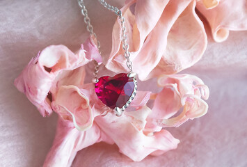 ewelry. Metal chain (necklace) with stylish pink heart pendants on soft silk fabric. Petals of rose creating, tender, romantic atmosphere. Valentine's day,  mother's, woman's day, love holidays.