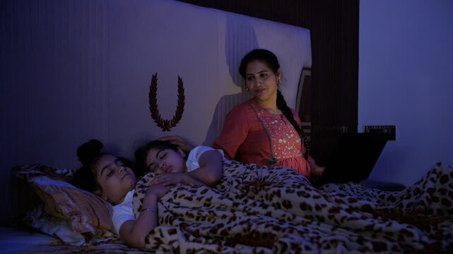 A young businesswoman working on a laptop - late night office work  stressful job  overtime  a caring mother. Adorable Indian siblings sleeping together covered under a blanket - family bonding  be...