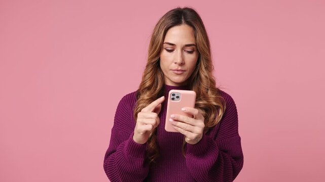 Sad upset young woman wear purple knitted sweater casual clothes hold use mobile cell phone swear read bad fake news unexpected rumor has some problem isolated on plain pastel light pink background