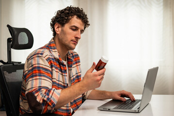 Young man using laptop for searching details about his prescribed medication while sitting at his cozy home.	