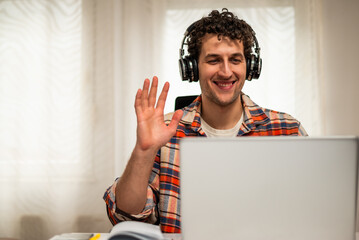 Smiling young man talking and waving during video call on laptop while sitting at his comfortable home.	