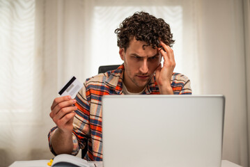 Worried entrepreneur using credit card and laptop at his home office. He is having problems with electronic banking while working remotely.	