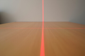 Red laser lines create a perfect crosshair on a light brown wooden surface, extending into a blurred background