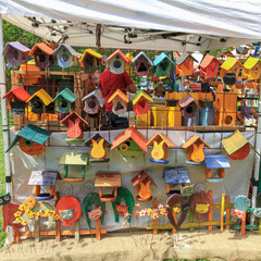 Bright wooden birdhouses and garden decor hanging at a street fair stall under a canopy. DIY handicraft, artisan marketplace, home and garden decoration concept.