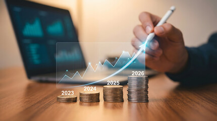 Professional hand highlights a glowing digital financial growth graph showing increasing coin stacks for 2023 through 2026 on a wooden desk with a lap