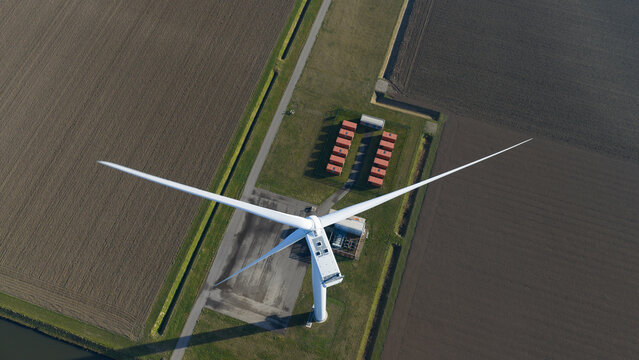 Aerial view of a solitary wind turbine standing tall against the backdrop of earthy fields and battery storage, Middelharnis, South Holland, Netherlands.