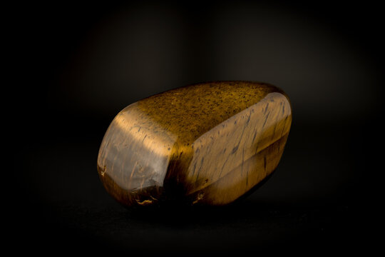 Polished tiger's eye gemstone with characteristic golden chatoyancy effect on dark background