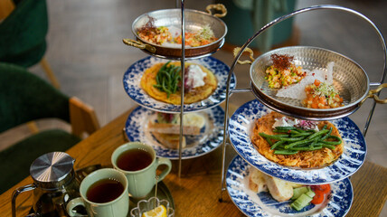 Fototapeta premium Elegant tiered stand displays savory crepes, fresh vegetables, and delicate appetizers with tea