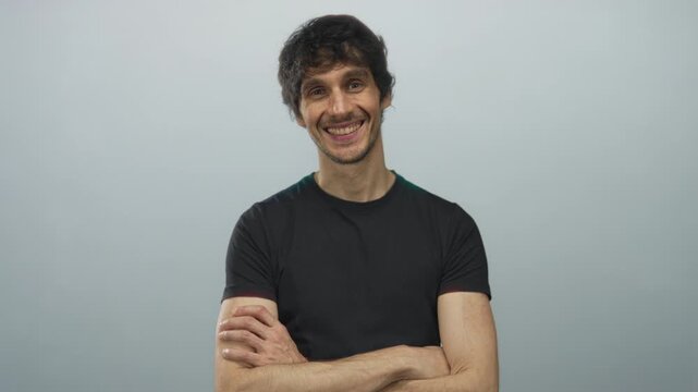 Man arms crossed in gray studio wearing casual black shirt and smirking gently; confidence strength poise.