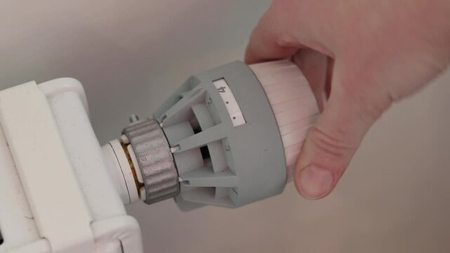 A woman's hand turns a mechanical thermostat on a radiator. A close-up of a temperature regulator on a battery. A mechanical thermal head of a battery regulator with a scale from 0 to 5