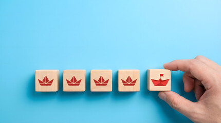 A human hand picks a distinct wooden block with a red paper boat symbol standing out among several crown blocks on a bright blue background