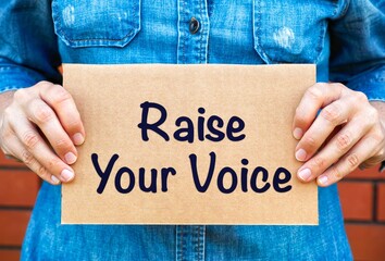 Woman holding a piece of a cardboard with words Raise Your Voice