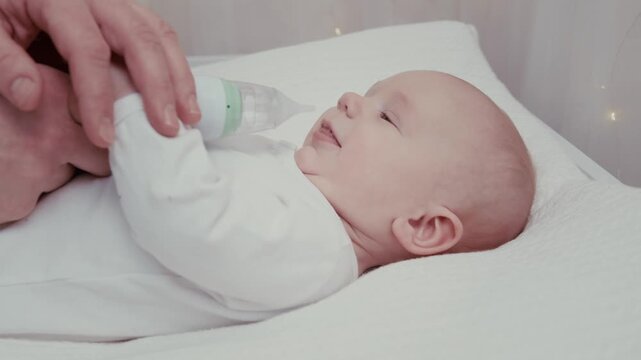 Attentive father carefully cleaning his infant son's nose with an electric nasal aspirator. Gentle parental care for a newborn with a runny nose to help him breathe easier during illness