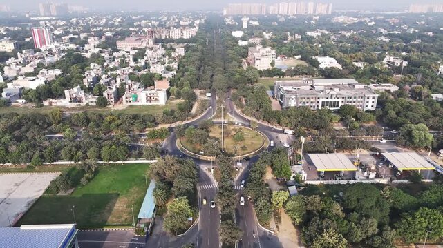 Top-down aerial of a Greater Noida roundabout, showcasing radial roads, moving vehicles, and dense green cover, symbolizing efficient connectivity within a planned urban landscape.