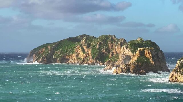 A stormy Mediterranean Sea after dawn. The sun's rays illuminate a rocky island battered by storm waves. Video slow motion 0.9x. Island of Mallorca, Spain.