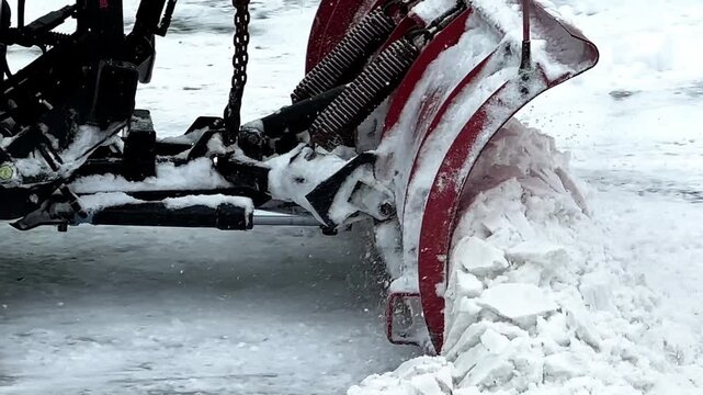 Heavy machinery with a red plow pushing slush and ice from a street during a winter snowstorm