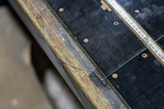 Miroitier professionnel rempla&ccedil;ant les verres d&rsquo;une tr&egrave;s vieille pendule au bois fortement ab&icirc;m&eacute;, mettant en valeur un travail de restauration artisanale sur un objet patrimonial.