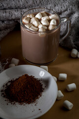 Warm cup of hot cocoa with marshmallows and cocoa powder on a wooden table during a cozy evening at home