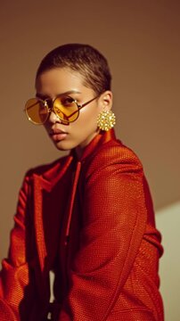 glam fashion portrait of a model in an oversized structured suit with a single bold gold accessory against a clean warm-toned background