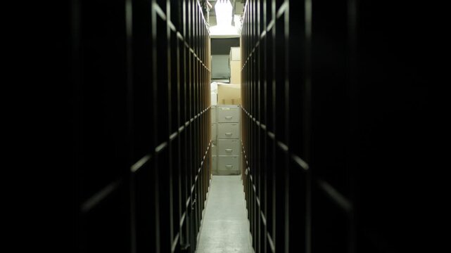 Exploring a dark storage area with shelves and filing cabinets in a narrow hallway