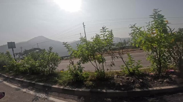 POV driving on a scenic four-lane highway towards Himalayan mountains on a sunny day in India.