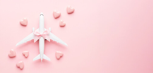 Airplane model with a pink ribbon surrounded by pink heart-shaped decorations on a pastel pink background, concept for travel with space for text