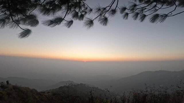 Cinematic 4K Ultra HD time-lapse video of swaying pine trees silhouette against dramatic orange sunset sky with moving clouds in the Himalayan mountains forest landscape of India during golden hour 