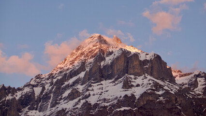 Snow-covered mountain peak with orange sunset light and clouds