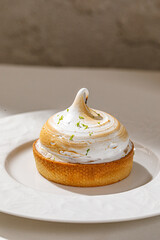 Lemon tart topped with toasted meringue and citrus zest served on elegant white plate