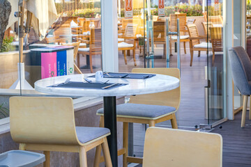 Empty table with chairs in a modern outdoor cafe or restaurant terrace. Minimalist dining area with wooden chairs and marble table, prepared for guests
