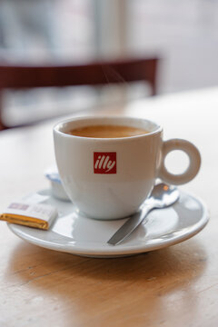 January 23, 2026, Amsterdam, Netherlands - Steaming Illy espresso cup with spoon and chocolate on a wooden table