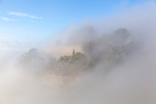 Lombardy Castle surrounded by misty fog in Enna, Sicily, Italy, showcasing ancient stone walls and lush greenery under a clear blue sky
