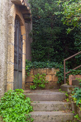 Naklejka premium Stone staircase leading to a rustic entrance with a wrought iron gate, surrounded by lush greenery in Enna, Sicily, Italy, showcasing traditional architecture