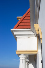 Naklejka premium High-contrast architectural detail of a white building corner with classical columns and a red tile roof against a blue sky
