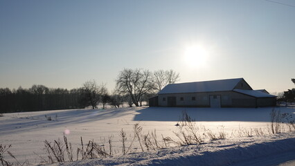 Krajobraz zimowy na wiejskim terenie podczas zachodzącego słońca. Zabudowania wiejskie w okresie zimowym podczas zachodu słońca. © tomo81