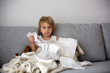 Blond toddler child, wiping his nose in a tissue, sneezing and coughing