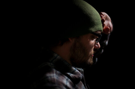 Close-up side view of a depressed man wearing a beanie with his hand on his forehead