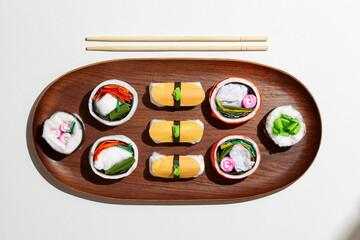Set of paper sushi on a wooden plate over white background. Top view with copy space. Pure and fresh concept and composition.